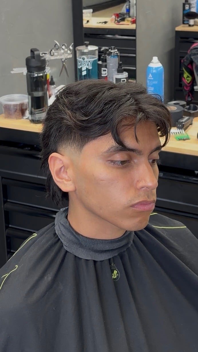 Man with dark textured hair and fresh fade haircut wearing black barber cape in salon setting