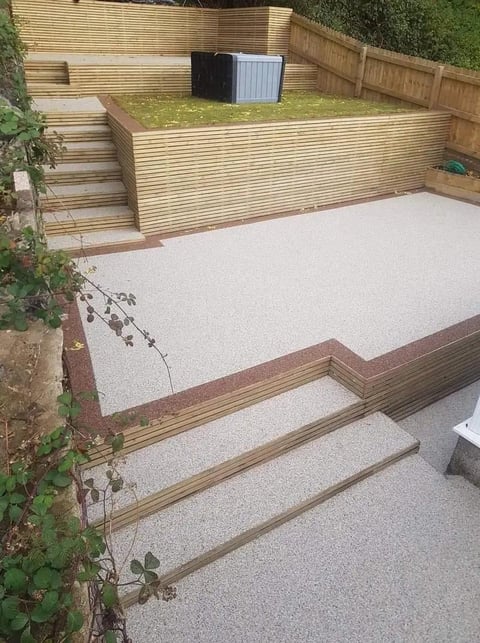 Modern backyard landscape with raised wooden deck, gravel patio, storage boxes, and tiered wooden retaining walls