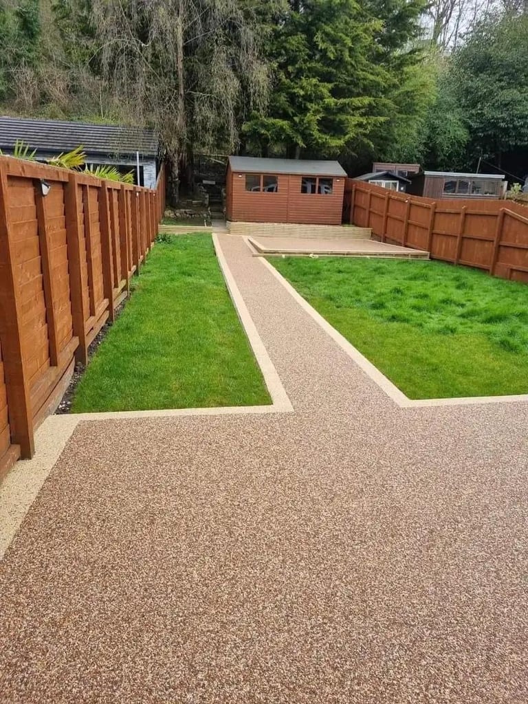 Residential backyard with wooden fences, green lawn, pea gravel pathways, and brick buildings surrounded by tall trees