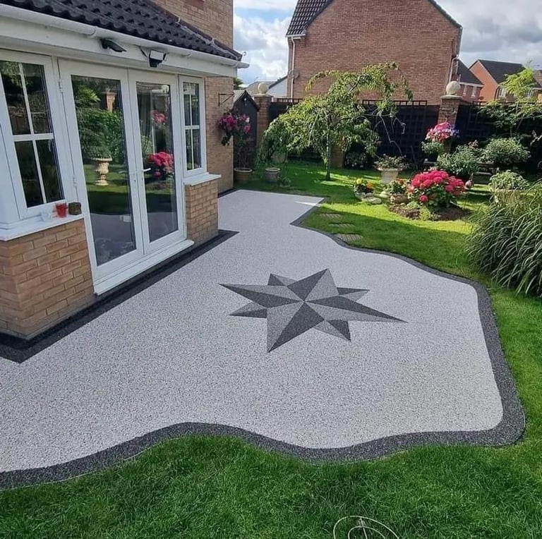Modern patio with gray composite decking featuring a star design, attached to brick house with white french doors, surrounded by manicured garden and flowering shrubs