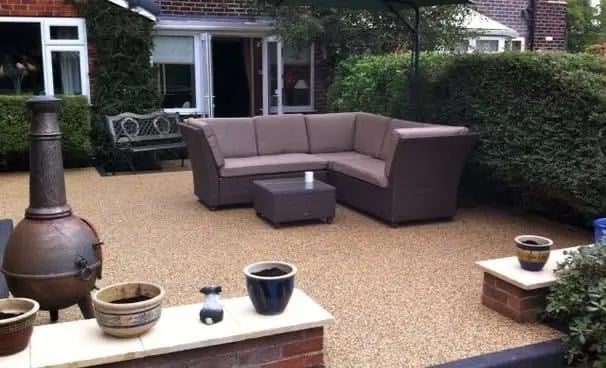 Outdoor patio with brown sectional sofa, coffee table, potted plants, decorative metal chimenea, and brick house in background