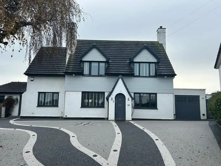 Modern white and black cottage with mansard roof, dark windows, and curved driveway lined with white stones