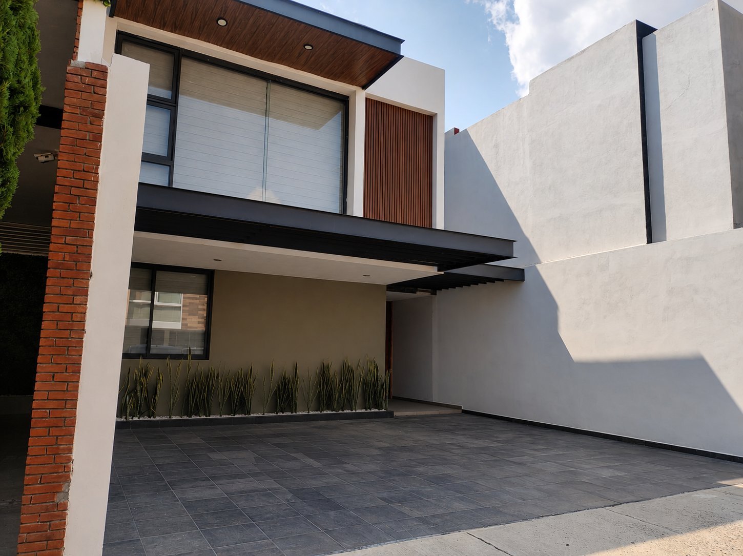 Fachada moderna de la casa de dos pisos con exterior de ladrillo y concreto, cochera techada, ventanas amplias y jardín frontal minimalista