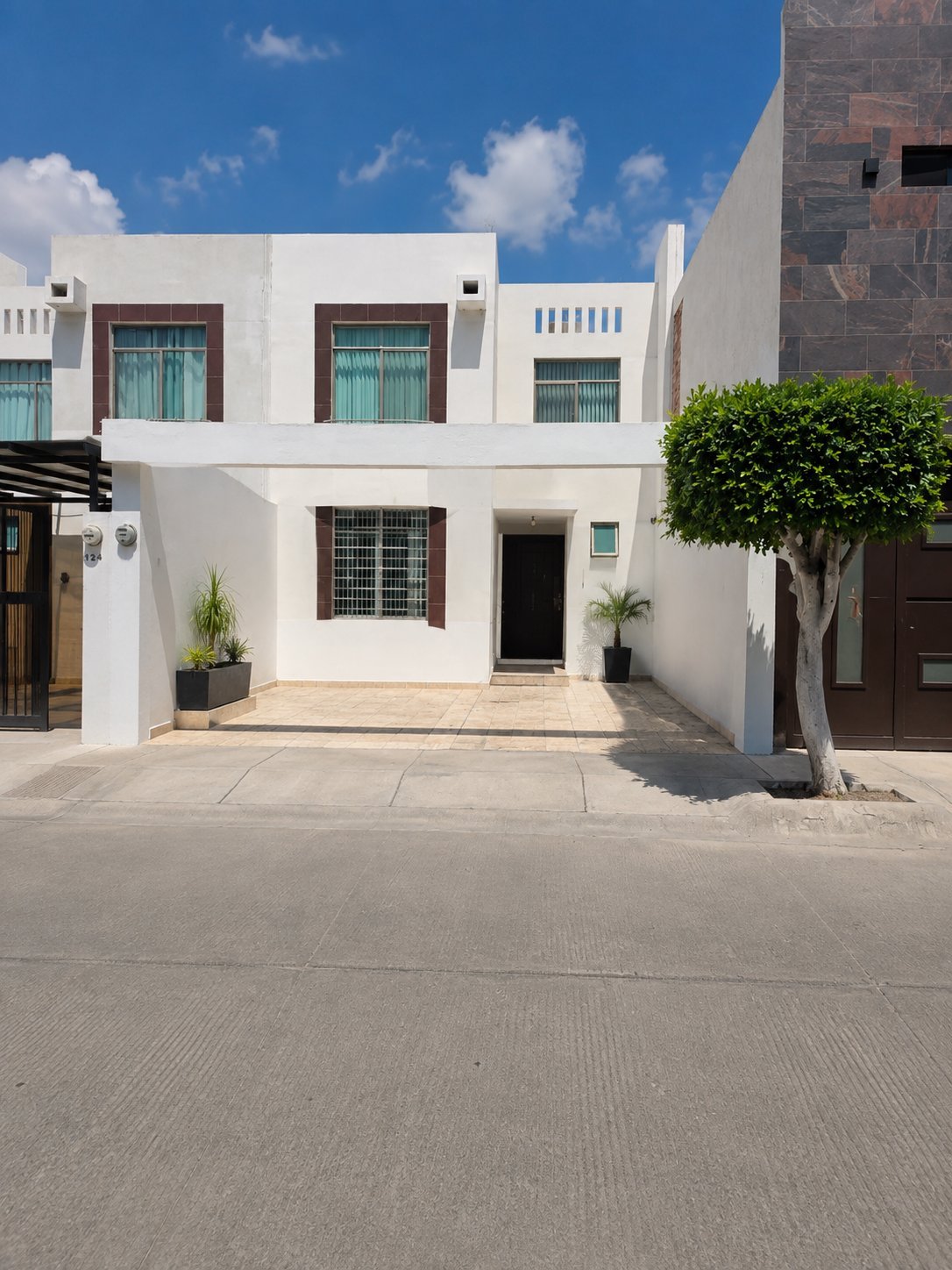 Fachada de la casa de dos pisos color blanco con marcos turquesa, balcón superior, cochera de concreto con palmera y número 124