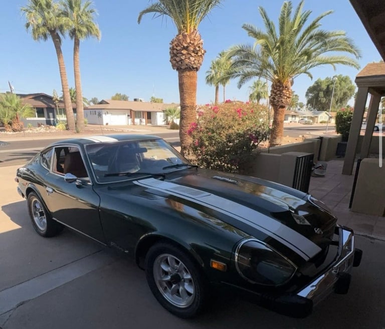 Black sports car with racing stripes parked in driveway with palm trees and desert homes in background