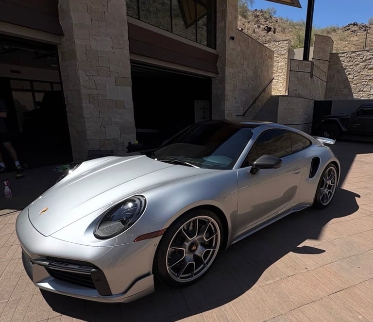 Silver Porsche 911 sports car parked in front of a modern concrete building in a desert setting