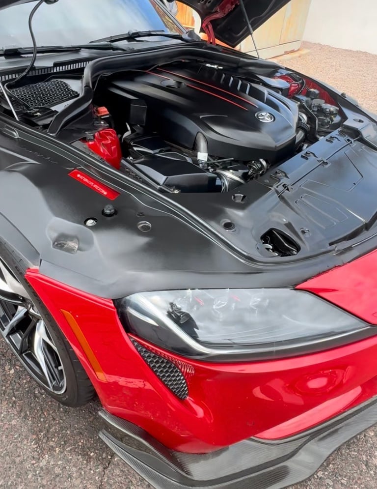 Red BMW sports car with open hood showing engine and black engine cover, headlight visible