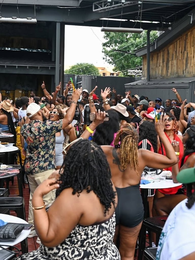 Large crowd of people dancing and celebrating with hands raised at outdoor venue