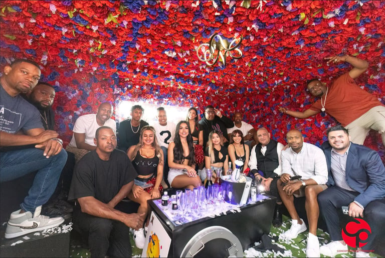 Group of people celebrating at a party with red and blue confetti overhead and a DJ booth in the center