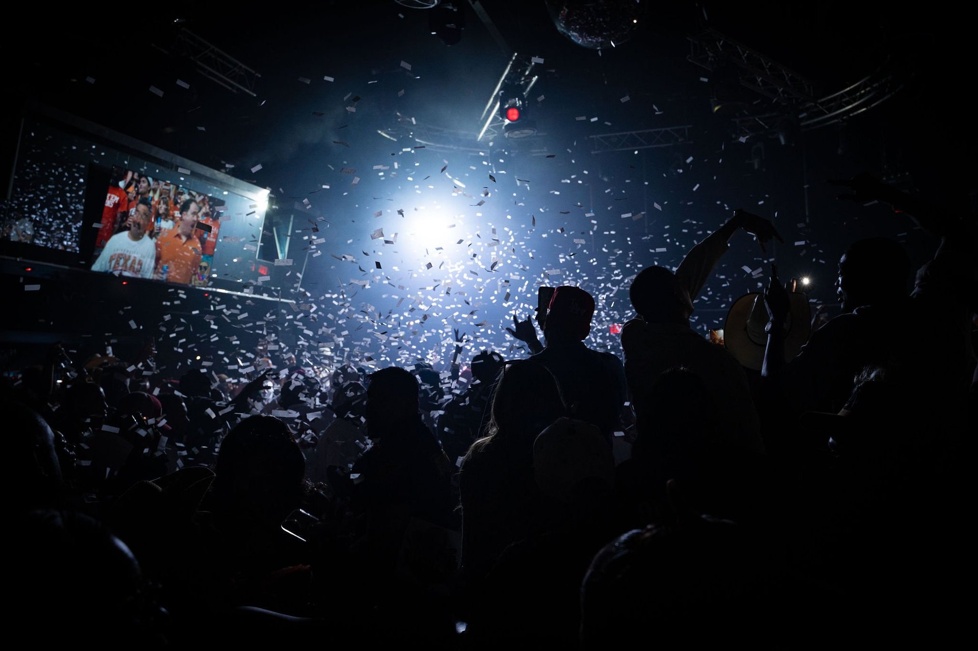 Crowd of concert-goers with raised phones at a live music event, stage lights illuminating the venue