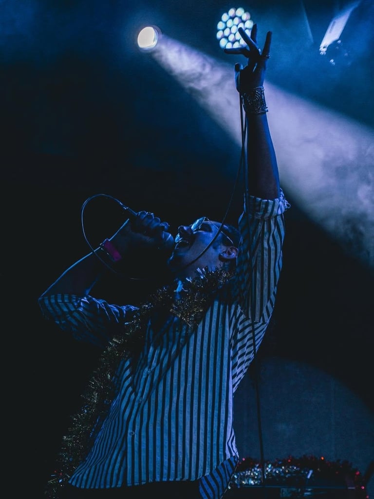 Zach Black on stage in a blue striped outfit with his arm raised toward the stage lights