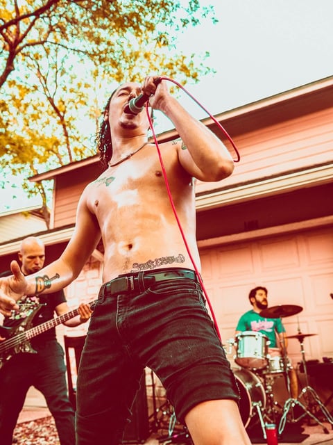 Shirtless male vocalist singing with band behind him outdoors