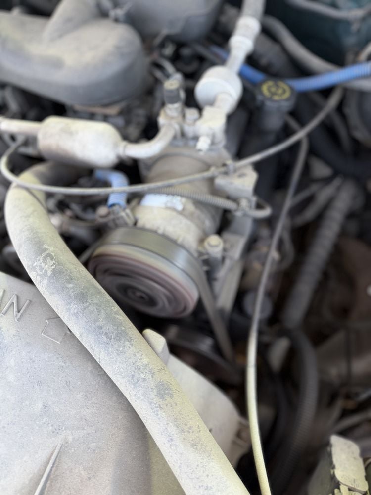 Close-up of car engine showing serpentine belt, pulleys, and hoses with dust and debris accumulation