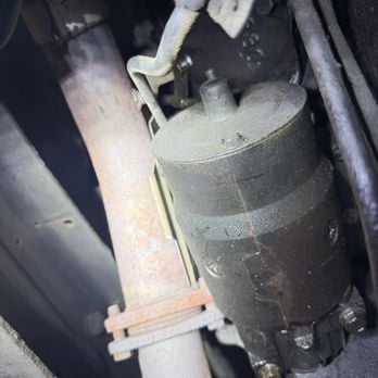 Close-up of a vehicle starter motor mounted on engine block with metal casing and white connectors