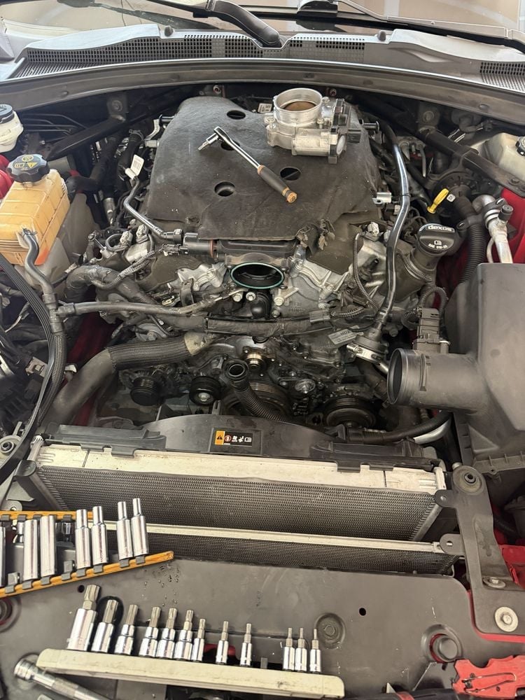 Open car engine bay showing motor, air intake, and various mechanical components