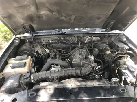 Open car engine compartment showing a dirty engine with visible components and intake manifold