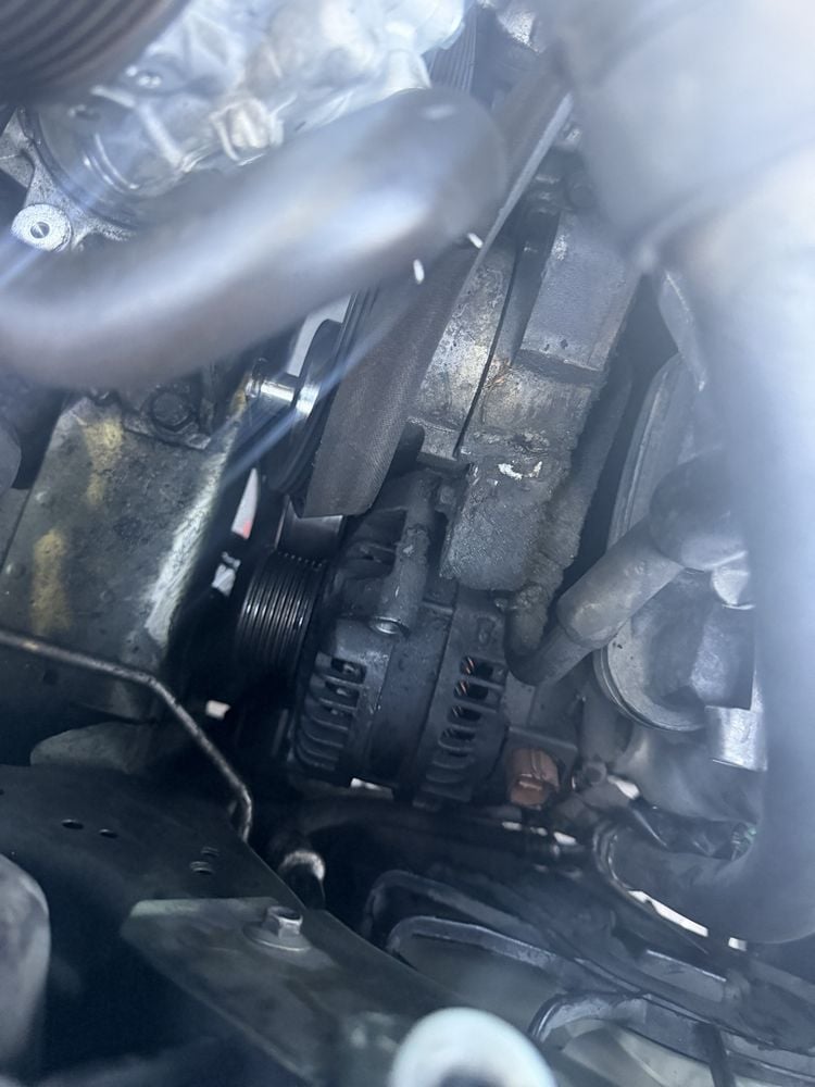 Close-up of a vehicle engine compartment showing the alternator, serpentine belt, and various engine components