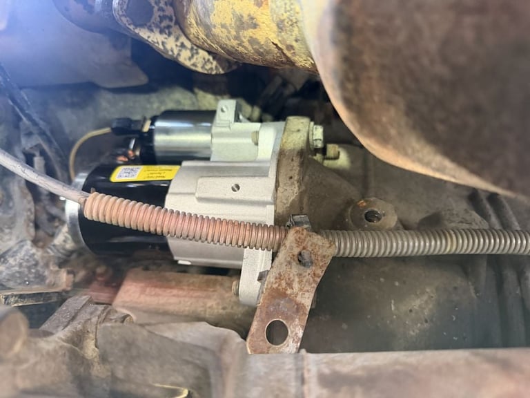 Close-up of a vehicle's starter motor and solenoid assembly with corroded components and attached wiring