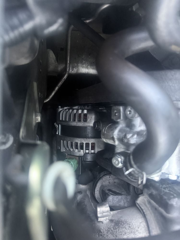 Close-up of a car engine showing an alternator with ribbed aluminum casing, cooling vents, and drive pulley