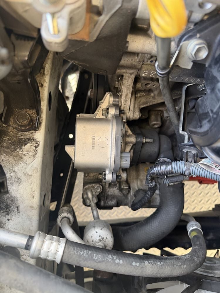 Close-up of an electric water pump mounted on a vehicle engine block with coolant hoses and electrical connector