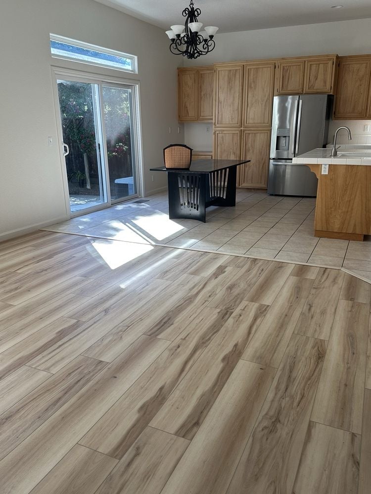 Spacious kitchen with wood cabinetry, stainless steel appliances, wood-look flooring, and glass doors opening to a patio
