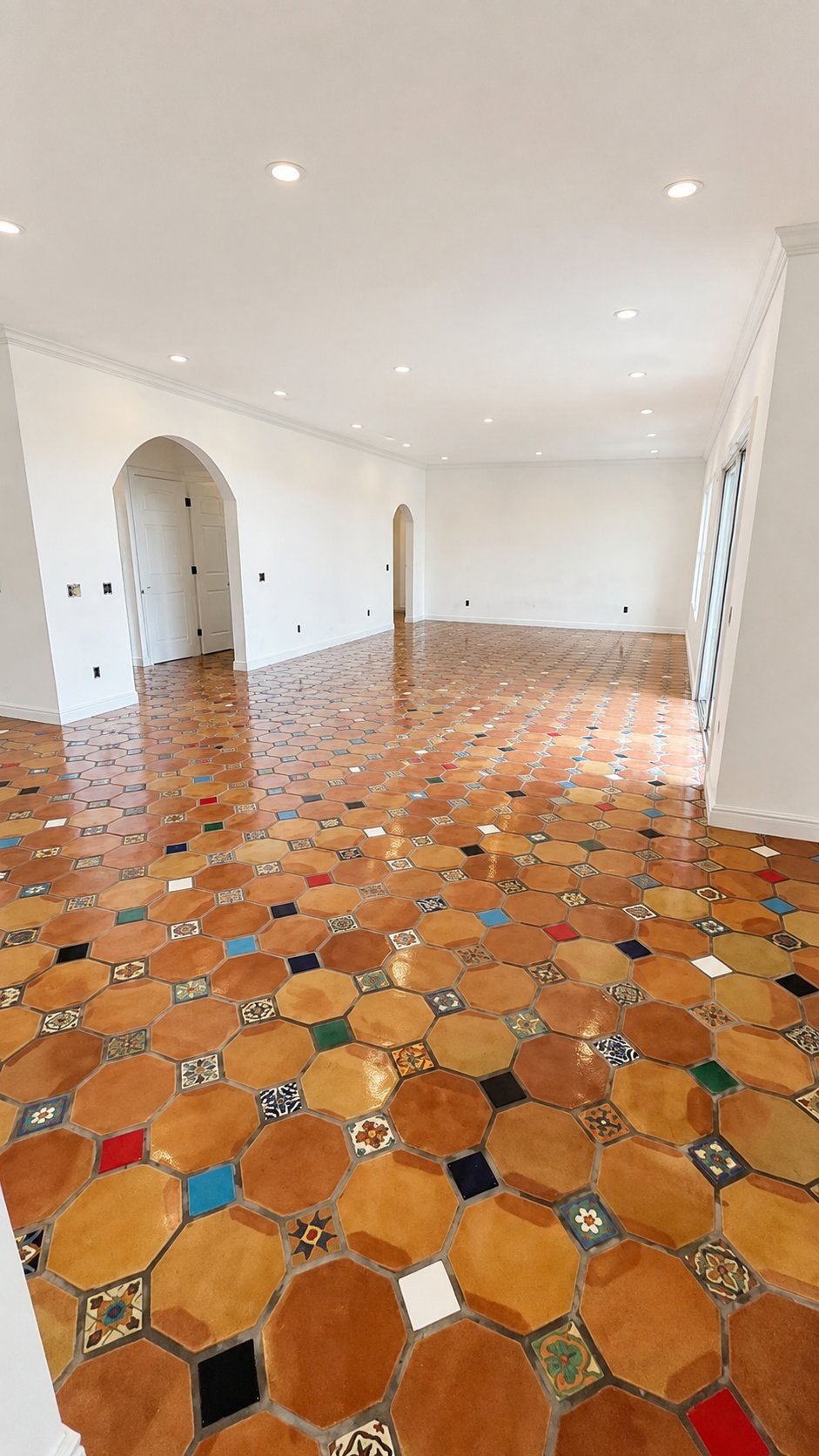 Empty room with terracotta hexagonal tile floor featuring colorful patterned accents, white walls, recessed ceiling lights, and arched doorway