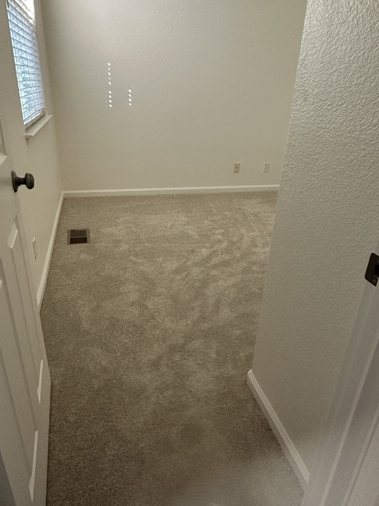Empty room with beige carpet, white walls, and door on left side
