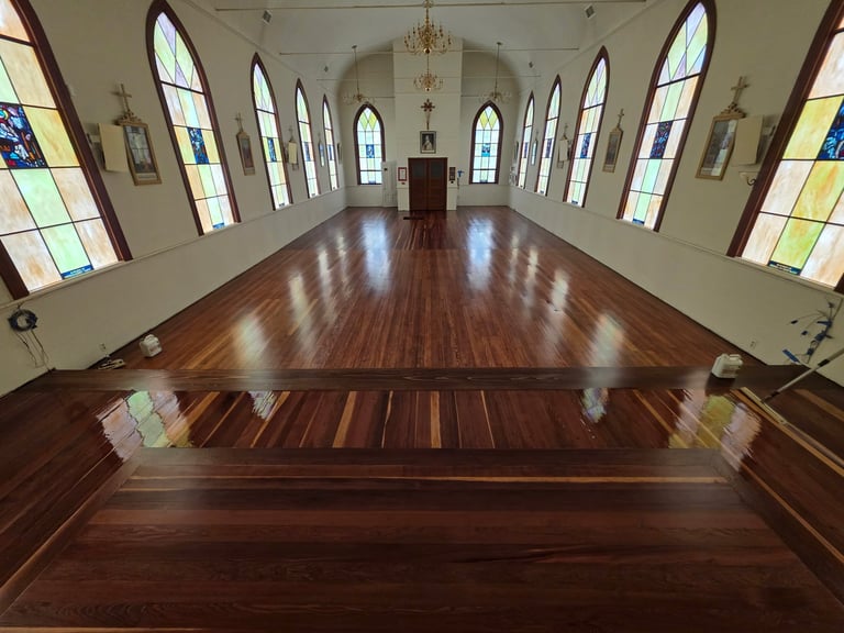 Interior of a church with newly refinished wooden floors, stained glass windows lining both walls, and altar at the far end