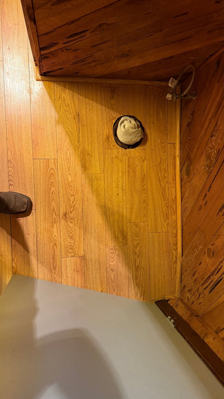 Rustic wooden cabin bathroom interior with honey-toned wood walls, ceiling, and flooring, straw hat on wall and white bathtub