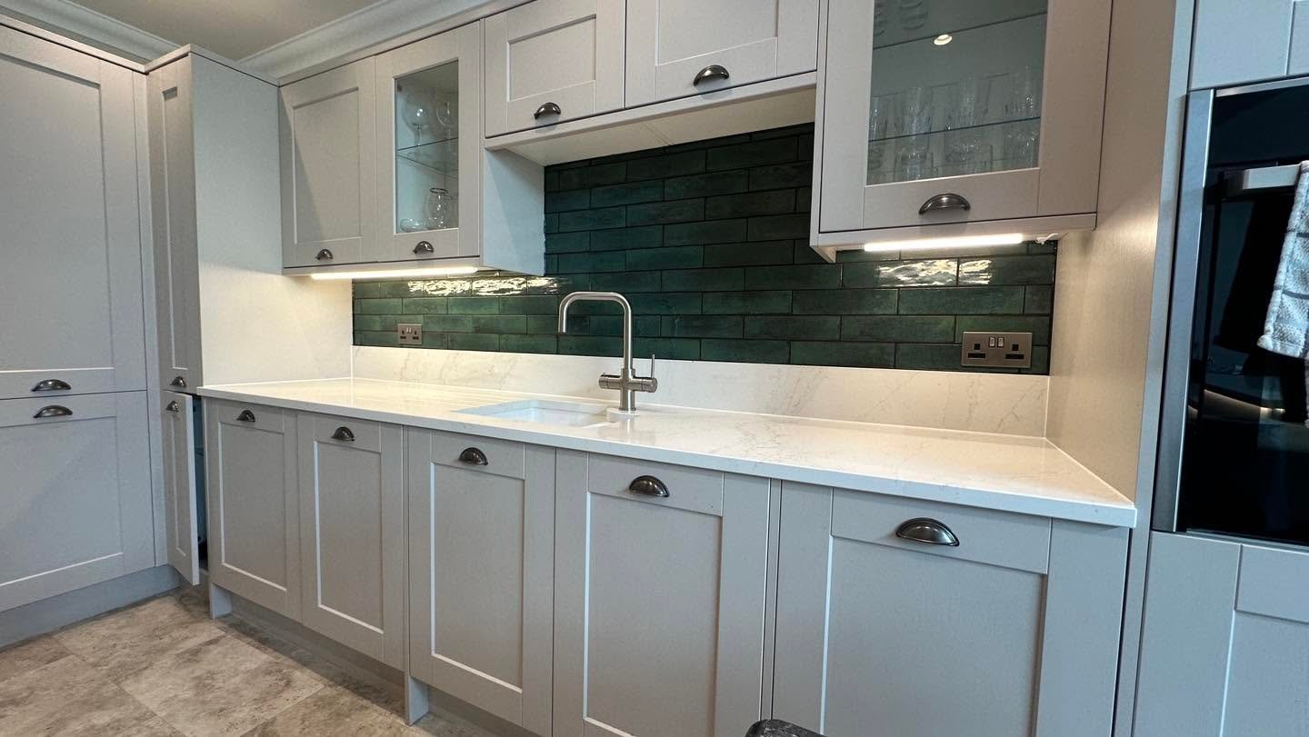 Modern white kitchen with dark green subway tile backsplash, white countertops, stainless steel sink, and black appliances