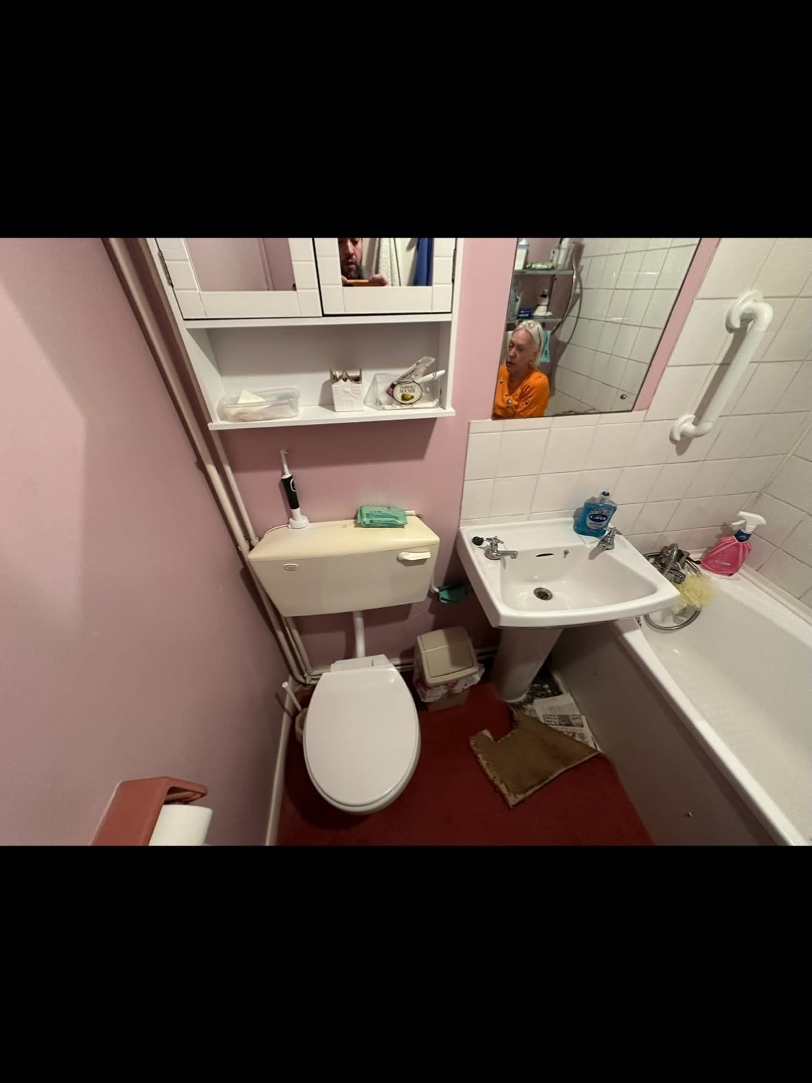 Small bathroom with pink walls, white toilet, pedestal sink, white tile backsplash, and bathroom fixtures on red tile flooring