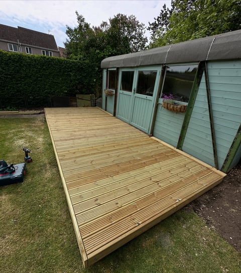 Wooden deck with pale blue-green garden shed in residential backyard with lawn and hedges