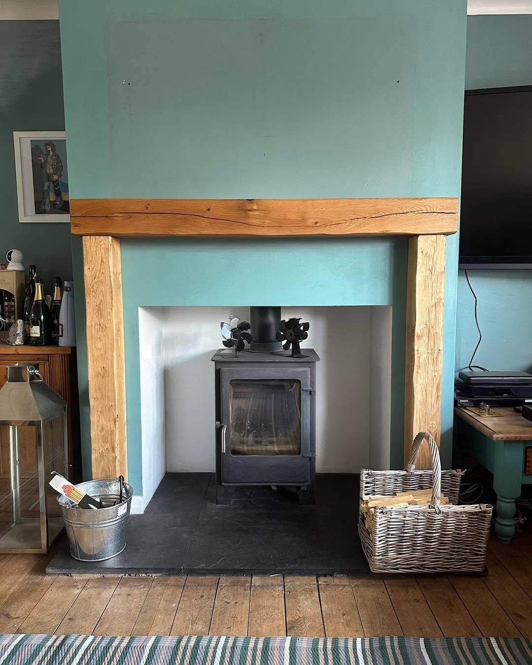 Modern fireplace with black wood stove in white alcove, wooden mantel, teal walls, and wicker basket beside hearth