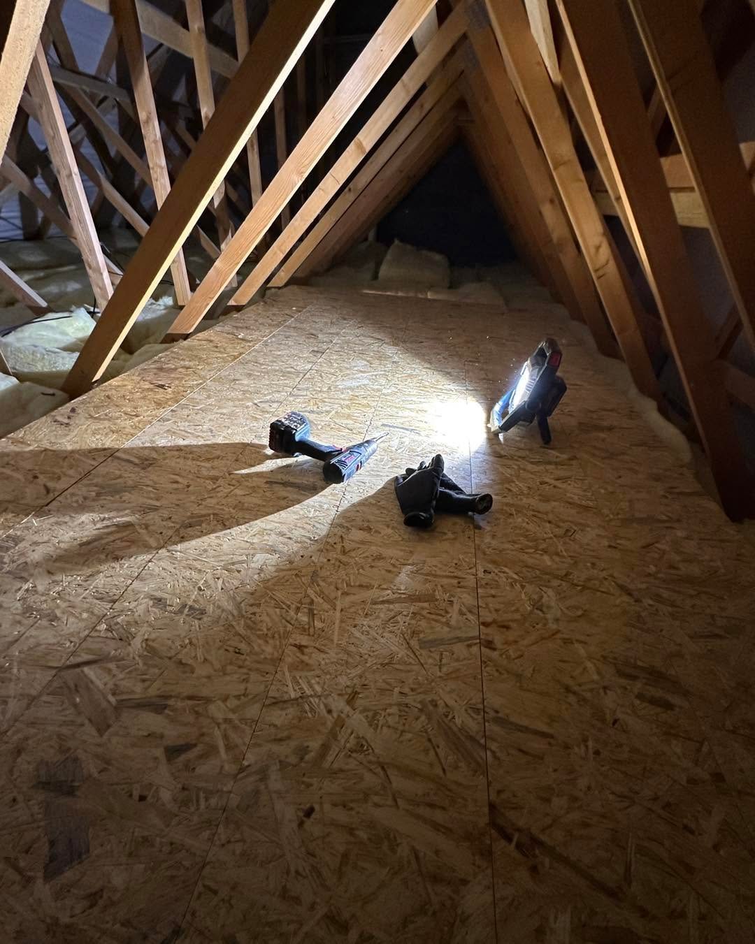 Person lying on OSB subflooring in attic space with wooden roof trusses above