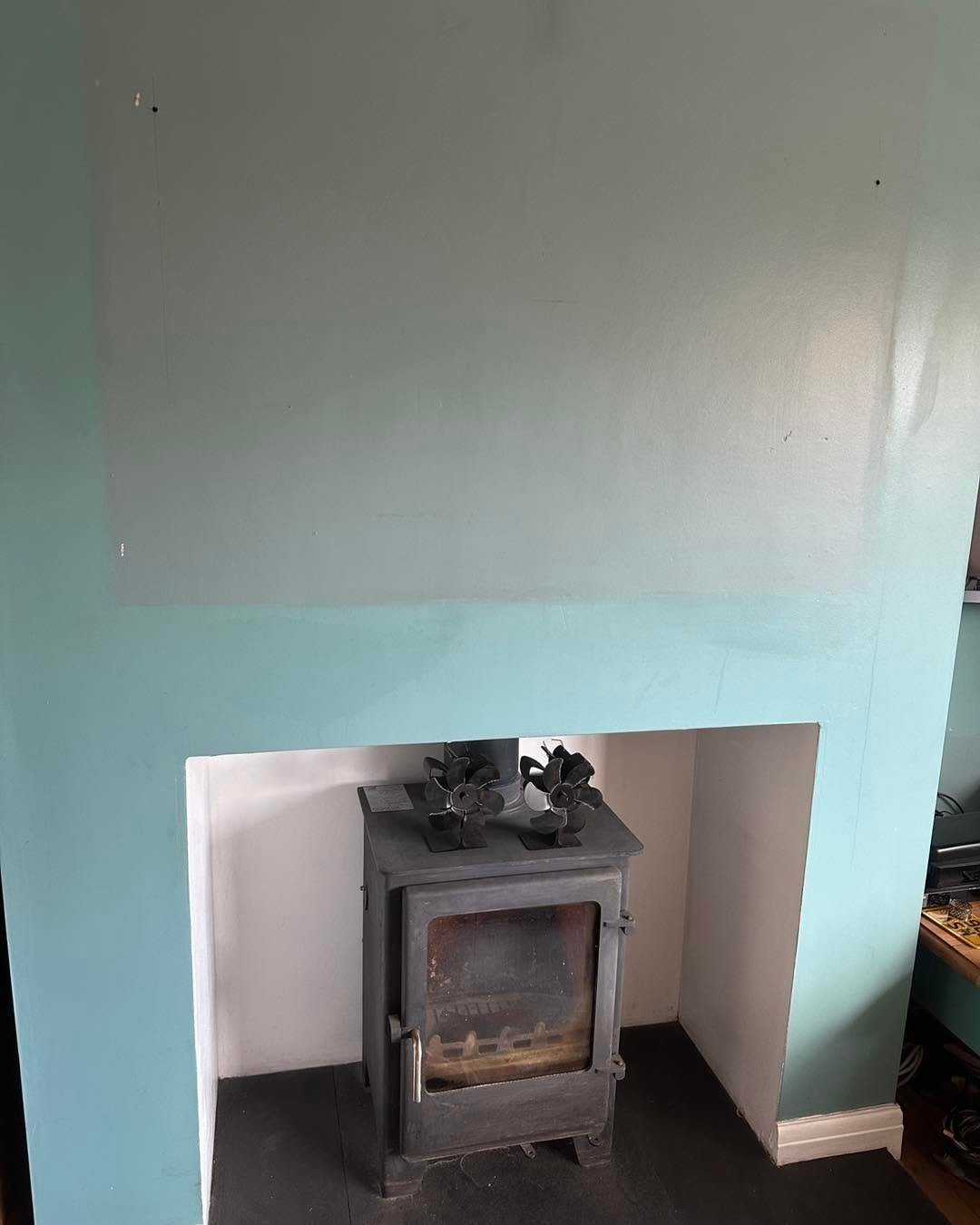 Black wood-burning stove with decorative items on top, set in a white alcove against a turquoise and gray painted wall.