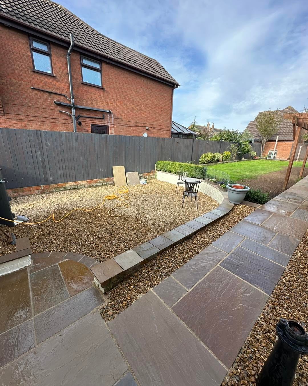 Backyard with red brick house, gravel area, paved patio, gray fence, and chair