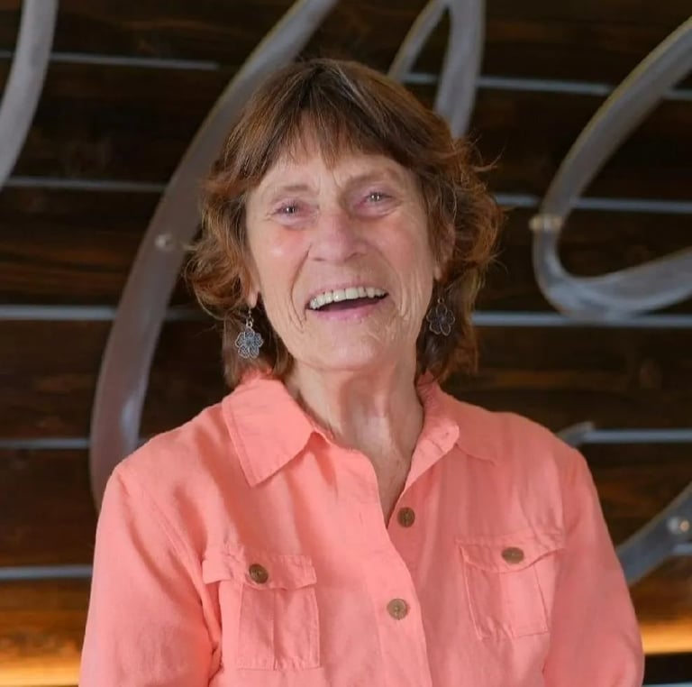 Smiling woman with shoulder-length brown hair wearing a coral button-up shirt in front of an industrial metal backdrop