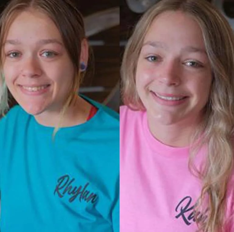 Two young girls smiling at the camera, wearing turquoise and pink t-shirts with text on them