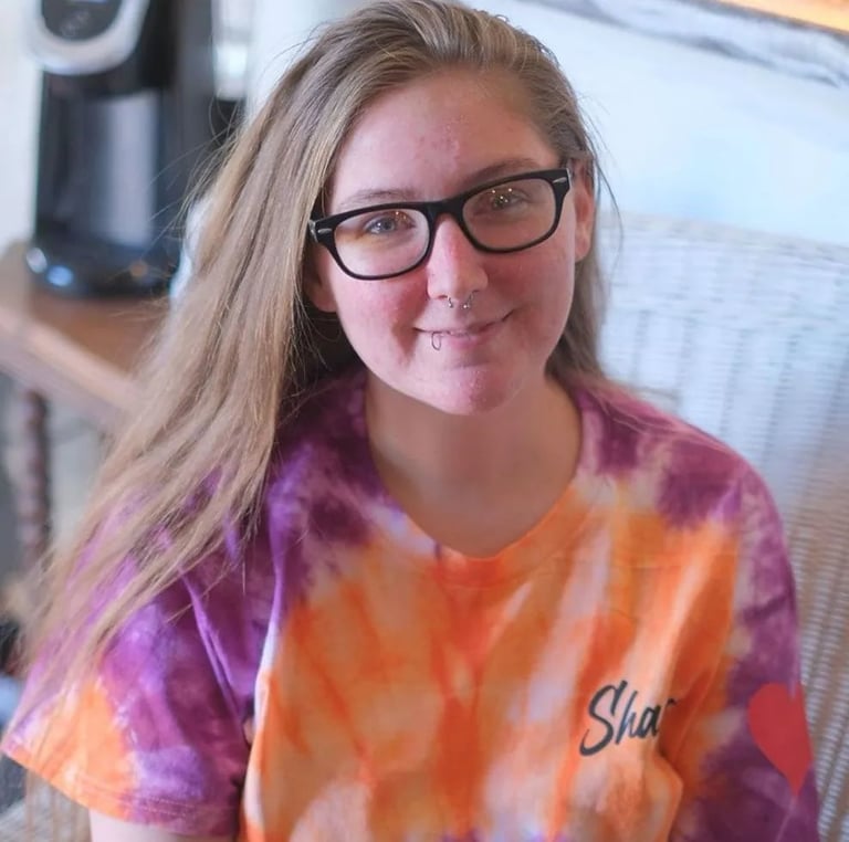 Smiling person wearing glasses and a tie-dye orange and purple shirt indoors
