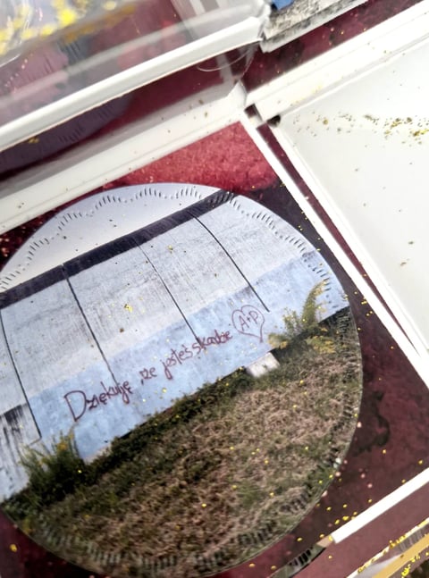 Overhead view of white paper plates with handwritten text stacked near maroon and white trim, on dusty ground
