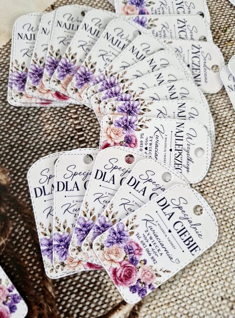 Collection of floral-printed wedding invitation tags with purple and pink flowers displayed on a neutral fabric background