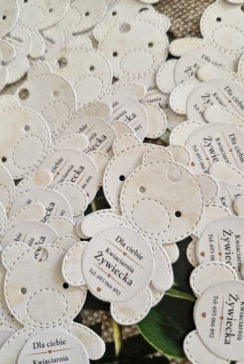 White scalloped plant tags with Polish text scattered together, showing seed labels with holes for attachment