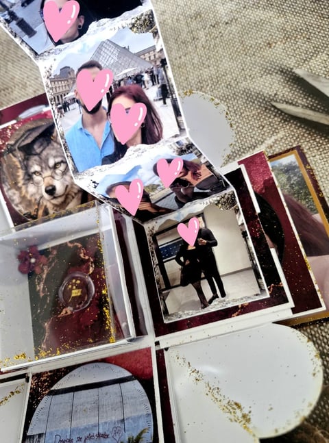 Scattered printed photos on a beige surface with pink heart stickers covering faces, including one of a wolf, arranged casually with a pen nearby