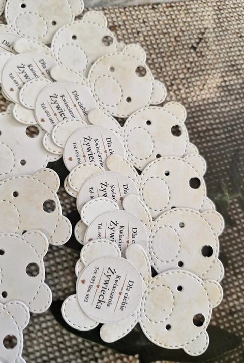 Collection of white scalloped product tags with text and perforated holes, arranged on beige fabric surface