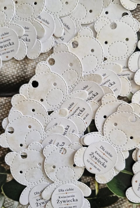 Collection of white scalloped plant tags with text and holes punched through them, scattered on display