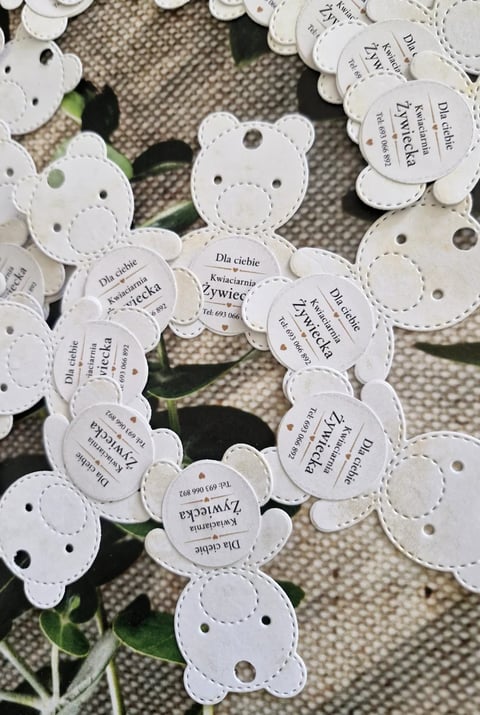 White scalloped paper bear-shaped gift tags with printed text arranged in a cluster on a neutral fabric background