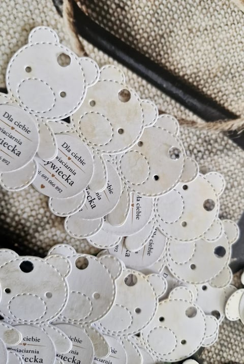 White button swatch cards with die-cut flower shapes and metal eyelet holes displayed on beige fabric