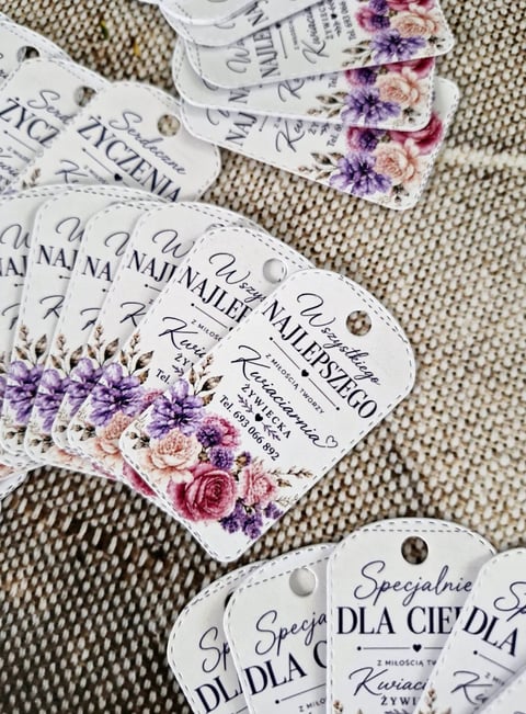 Decorative product tags with floral designs and Polish text arranged on a beige textured fabric
