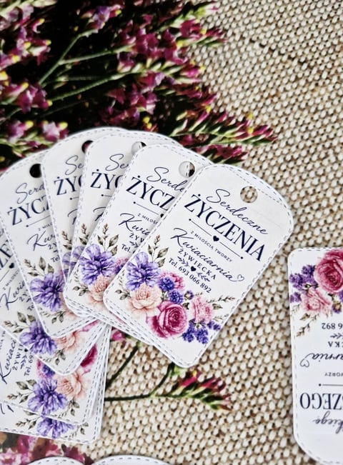 Multiple floral wedding favor tags with purple and pink flowers arranged on beige textured fabric with fresh carnations