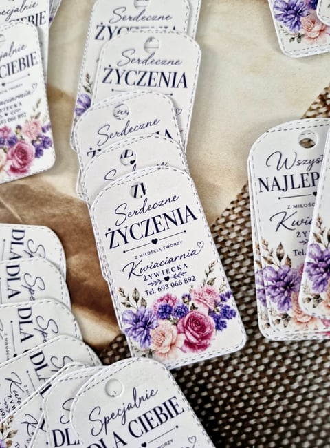 Decorative white gift tags with floral designs, featuring Polish text and purple and pink flowers, arranged on a textured surface